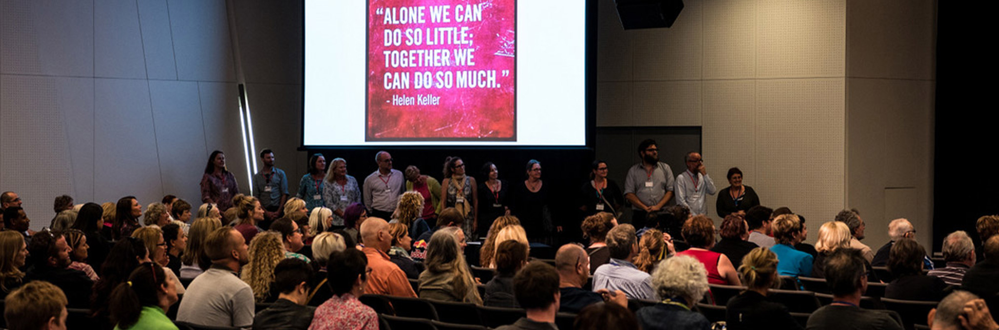 cru board and staff standing in line at the front of a conference under a slide that reads 'alone we can do so little, together we can do so much' by Helen Keller