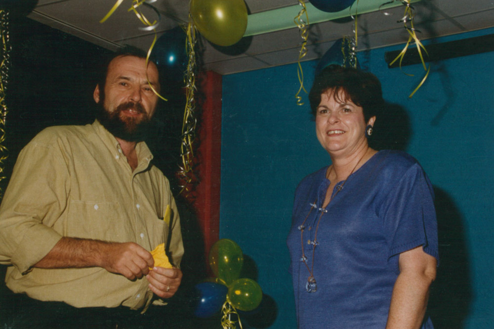 A man and a woman standing at a celebration, surrounded by balloons and streamers