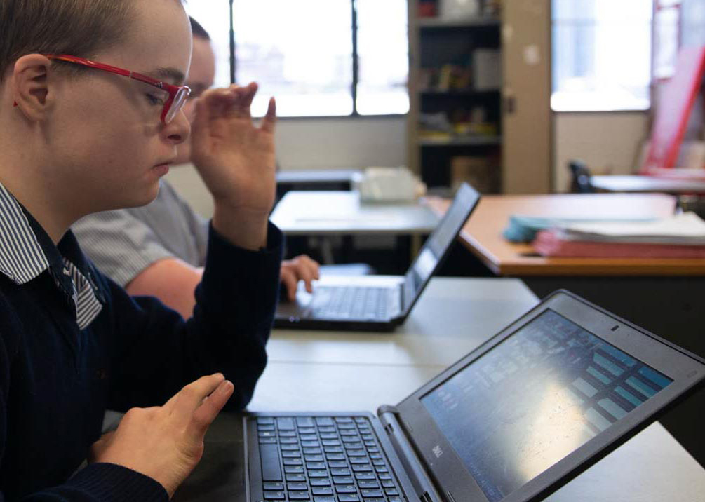 A young school boy wearing glasses working on a laptop