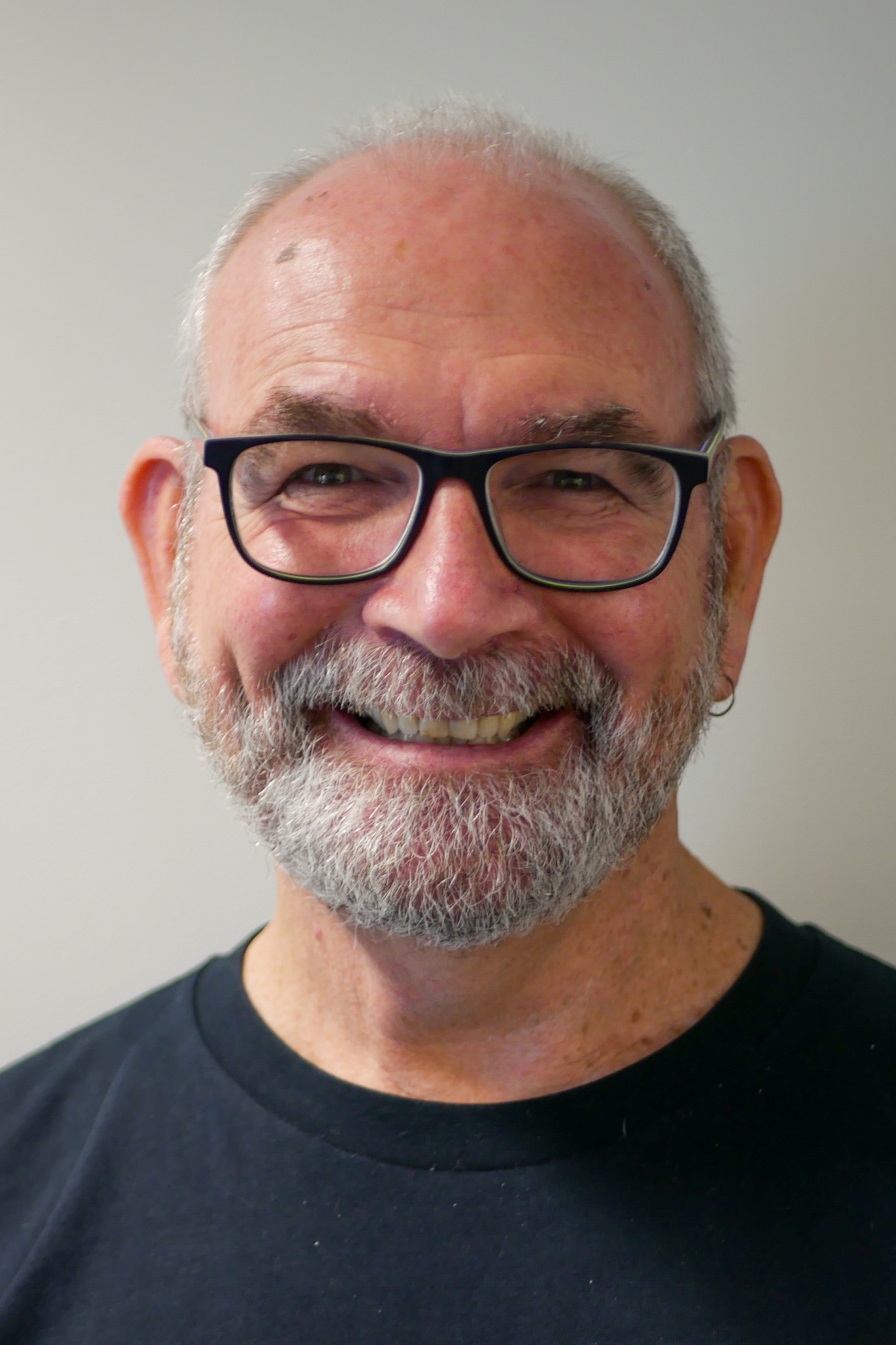 Jim wearing glasses and a black shirt, he has a short beard and is smiling.