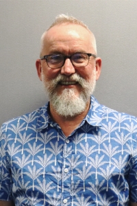 Matt with a grey beard, wearing glasses and a blue patterned shirt