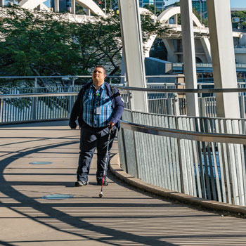 Blind man with white cane walks along bridge