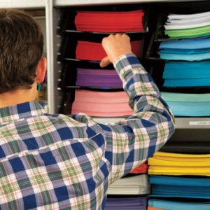 Picture of a man standing in front of a shelf full of stacks of different coloured papers