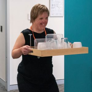 Woman with down syndrome carries tray of dishes