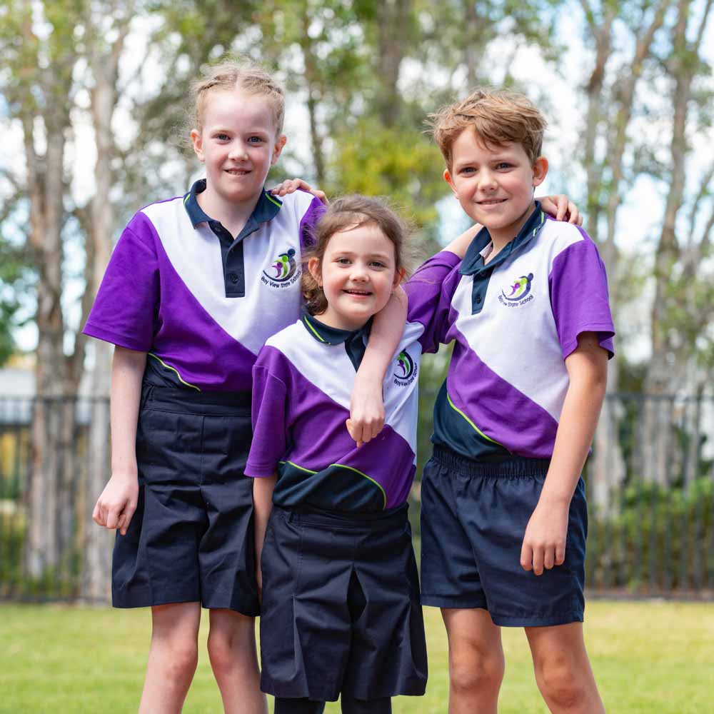 Three young kids in school uniform with their arms over each others shoulders