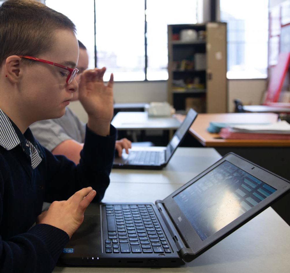 A student with down syndrome uses a laptop computer in class with his peers