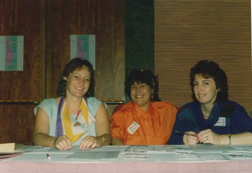 3 women sitting at a desk with sign in sheets and name tags