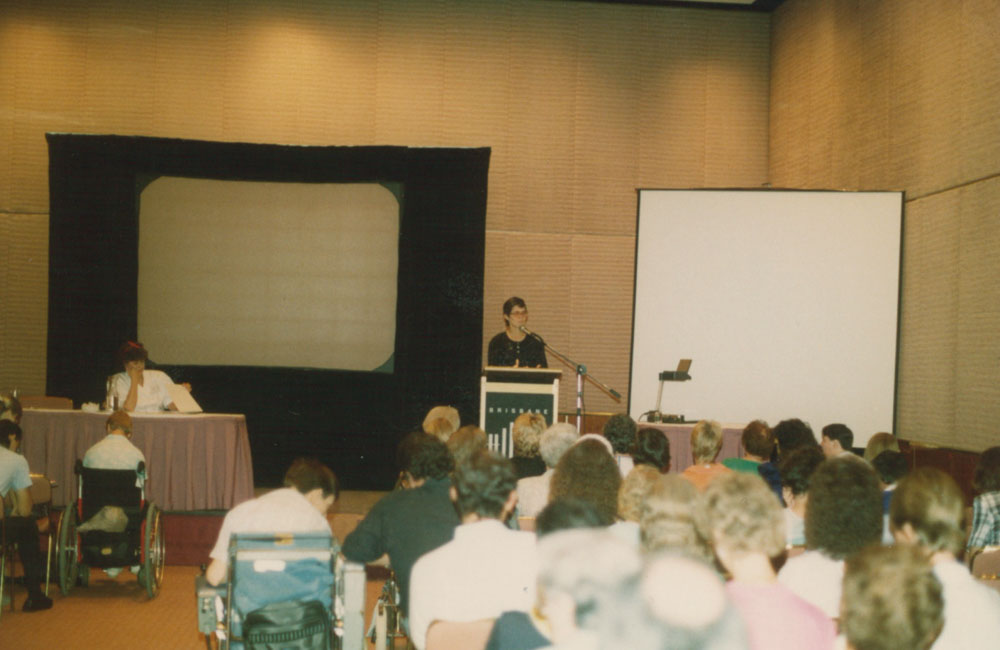 A lady speaking at a podium before a room of people