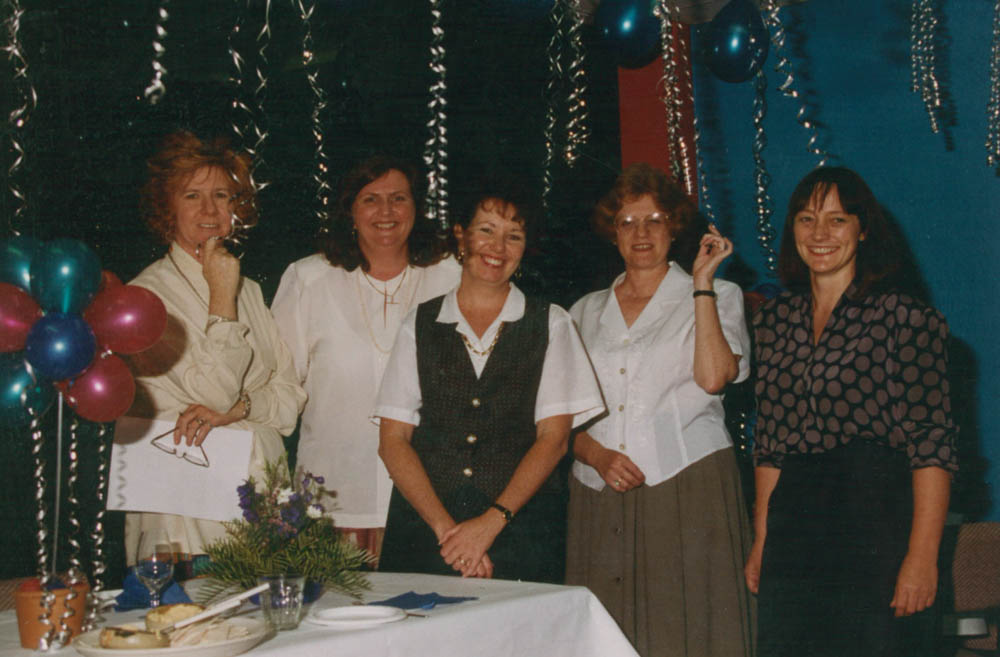 Five women standing together and smiling surrounded by streamers and balloons