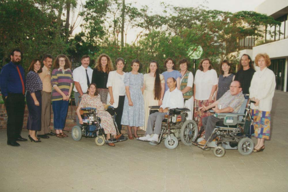 A group of men and women, three of whom are in wheelchairs, standing together and smiling