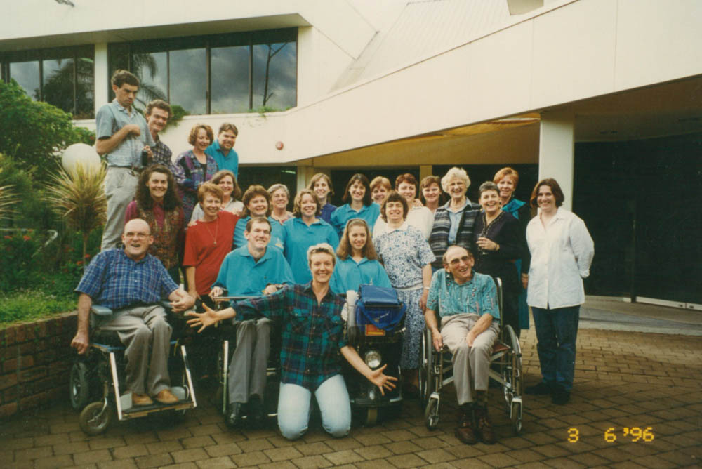 A group of people standing together and smiling. Men, women and many in wheelchairs.