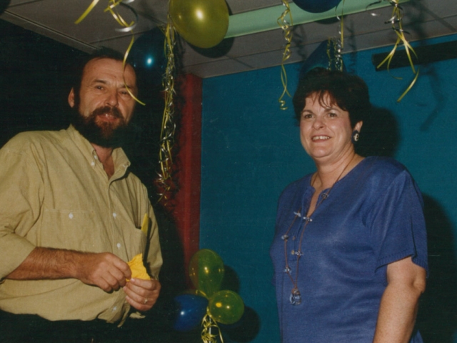 A man and a woman standing at a celebration, surrounded by balloons and streamers