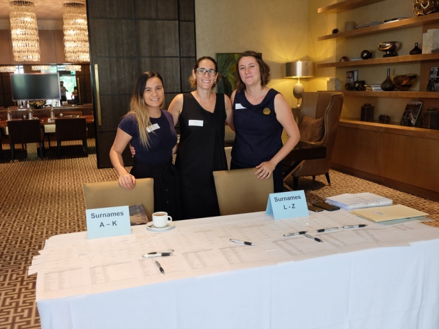 three cru staff members standing together at a conference venue in front of a table filled with name tags and sign in sheets