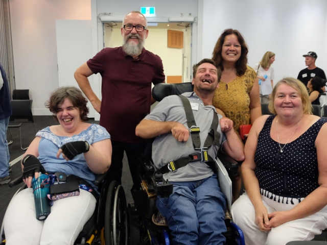 3 women and 2 men laughing and smiling at a cru event, surrounded by empty chairs at the end of the day.  Two of the people are in wheelchairs.