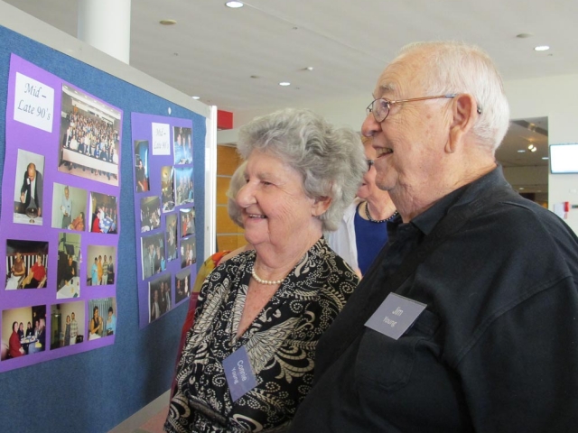 An older couple standing together looking at a board covered in photos.  It has the label 'mid to late 90's'.