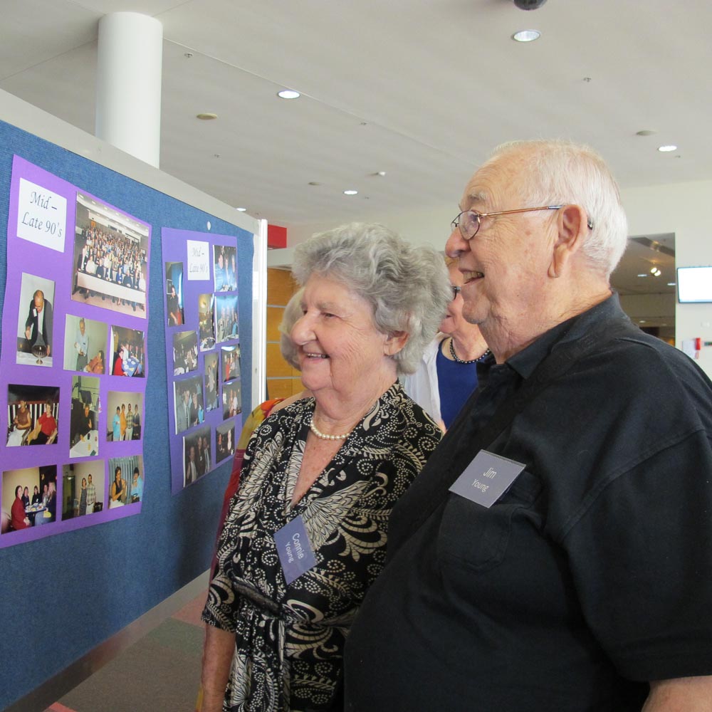 An older couple standing together looking at a board covered in photos. It has the label 'mid to late 90's'.