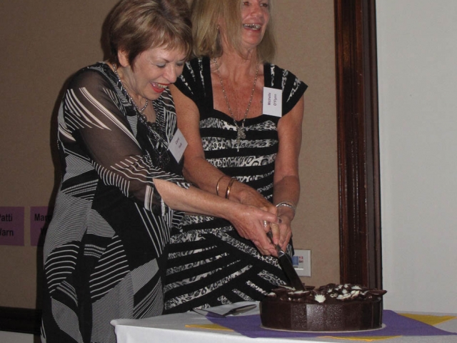 2 women holding the same knife, laughing and cutting a cake.
