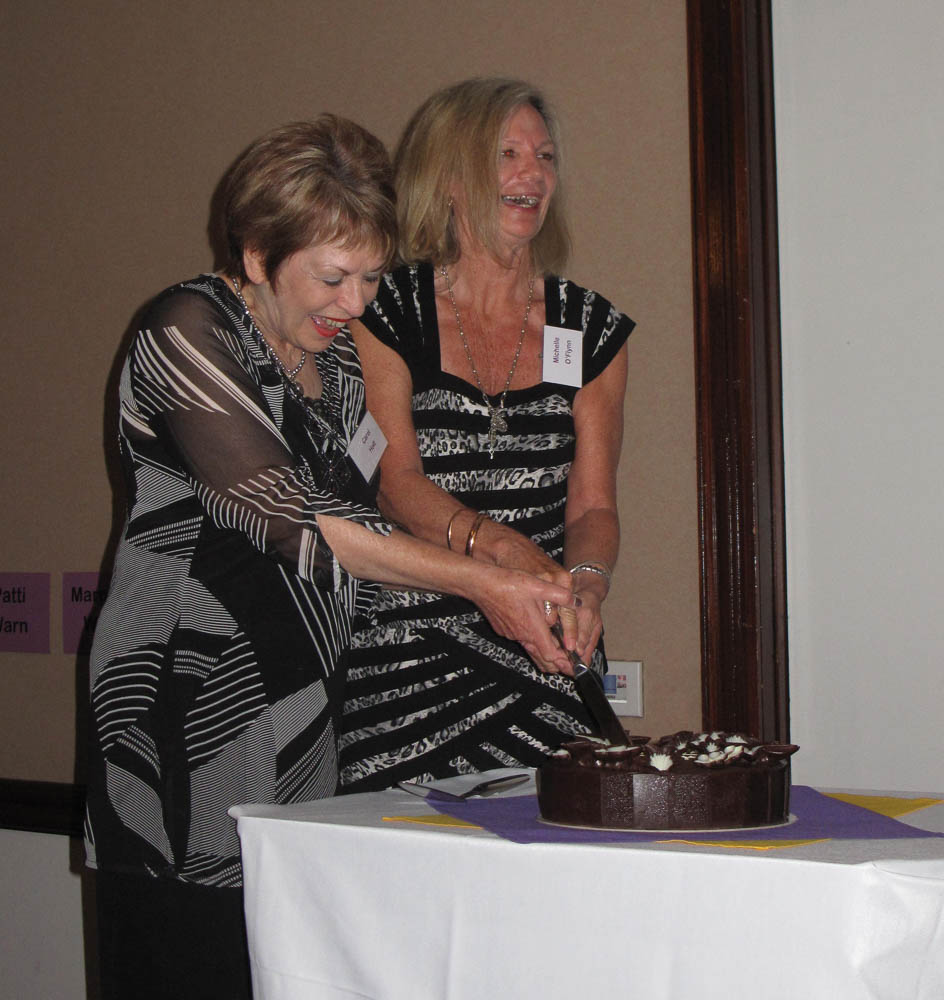 2 women holding the same knife, laughing and cutting a cake.