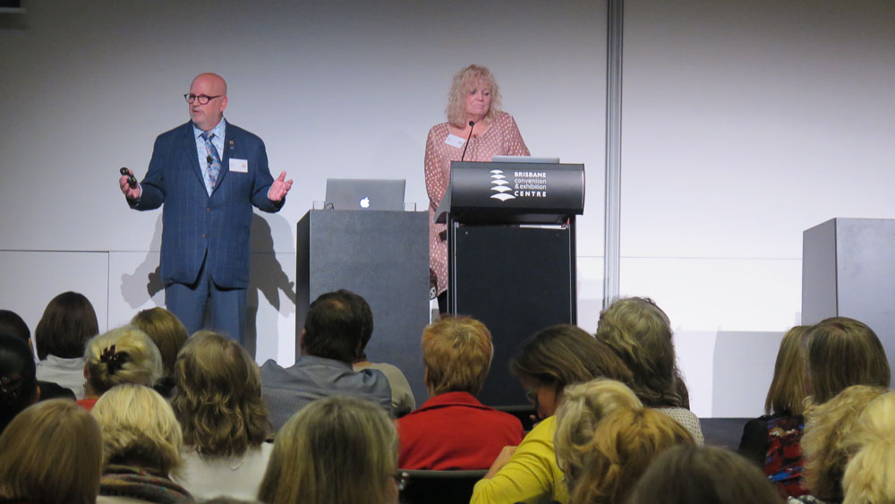 A man and woman from Canada presenting together in a full auditorium