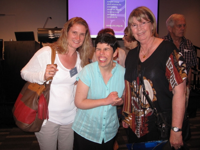 3 women at a conference standing together and smiling.  One of them has a disability.