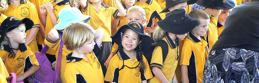 A photo of a group of school kids in bright yellow uniforms. In the middle is a girl with down syndrome smiling