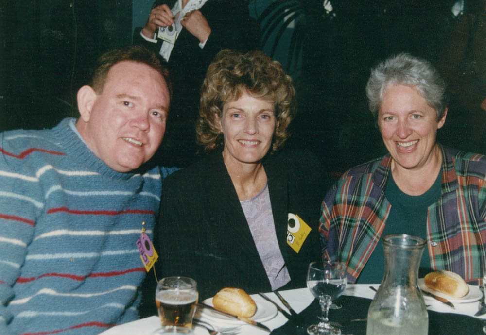3 people wearing name tags, sitting together smiling