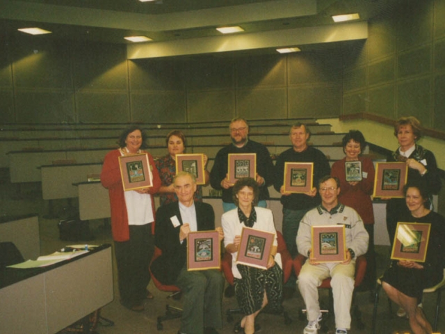 9 people sitting in an auditorium holding framed images