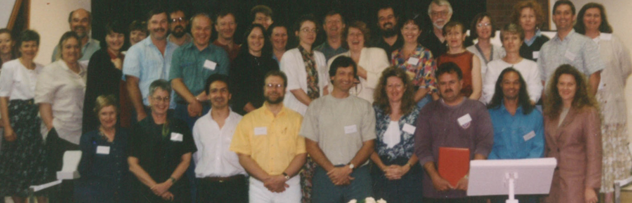 A photo from the mid 1990's of a large group of people at the end of a seminar. People are standing together with name badges on.