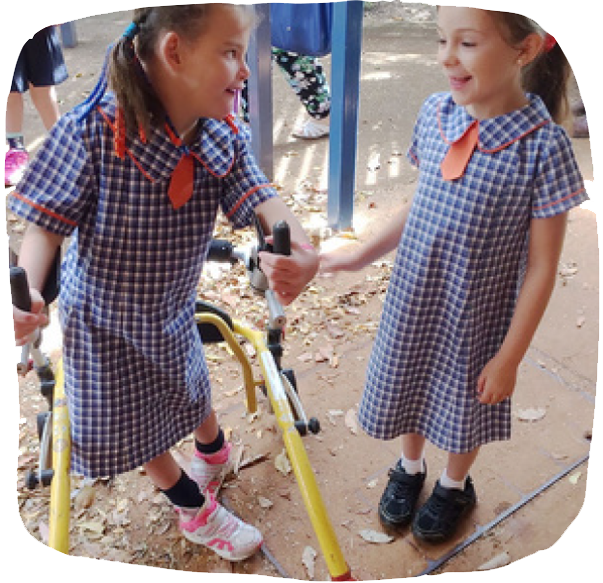 two young girls in school uniforms standing a smile at eachother. One of them has a mobility aid.