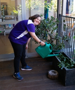 Woman wearing work uniform watering a pot plant.