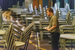 Man pushing a trolley load lifter moving a stack of chairs.