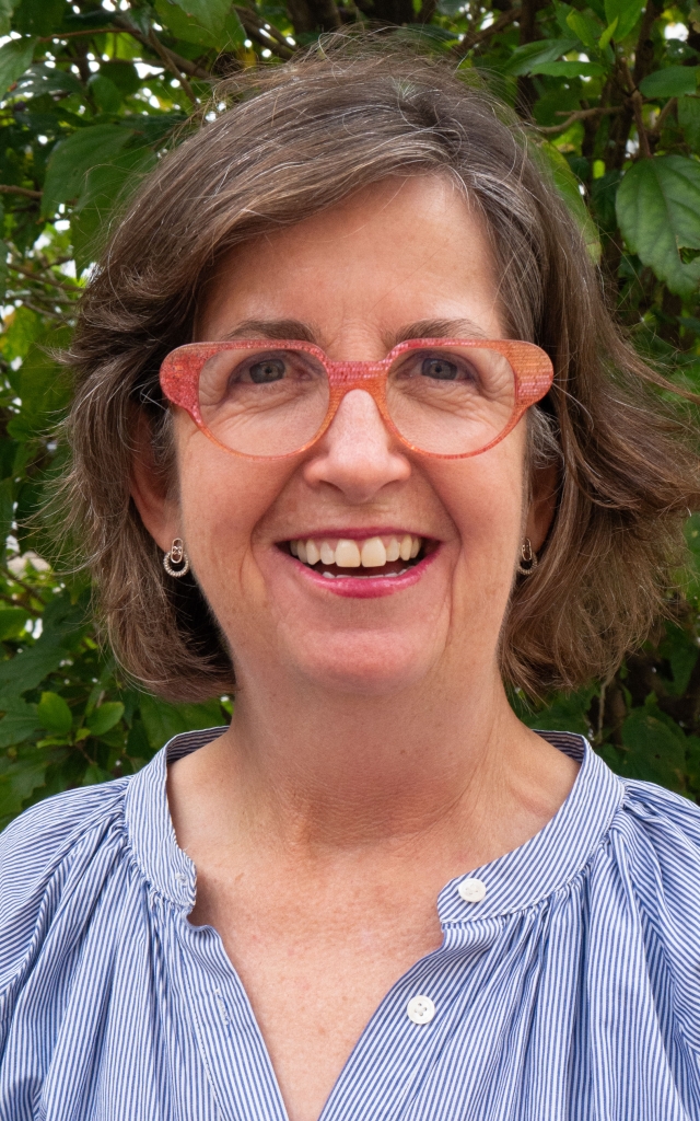 Anna Coventry wearing glasses and a blue shirt smiling.