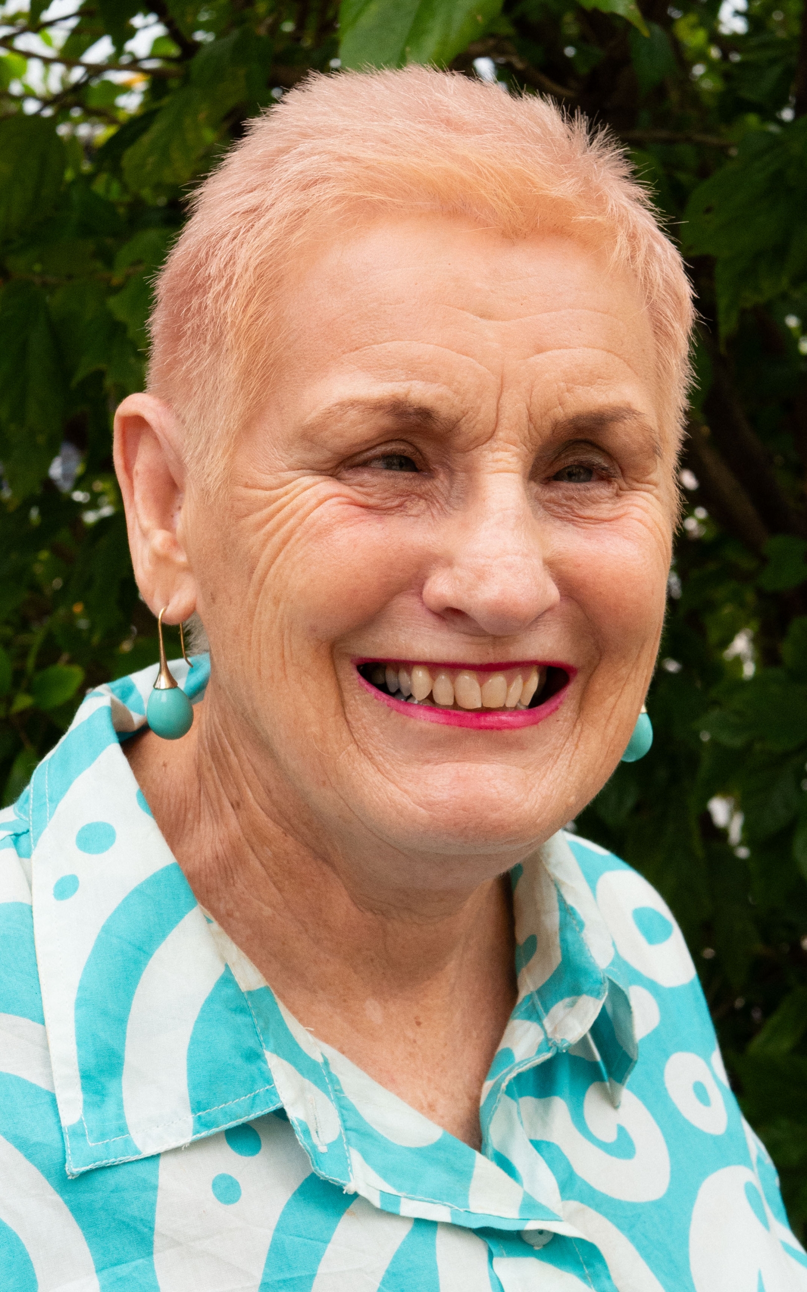 Josey McMahon wearing a blue and white shirt with earrings and smiling.