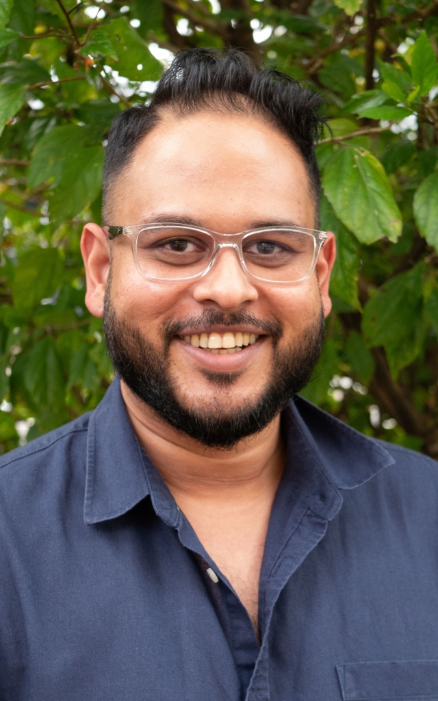 Naish Nand with short black hair and dark blue collard shirt and a beard smiling.